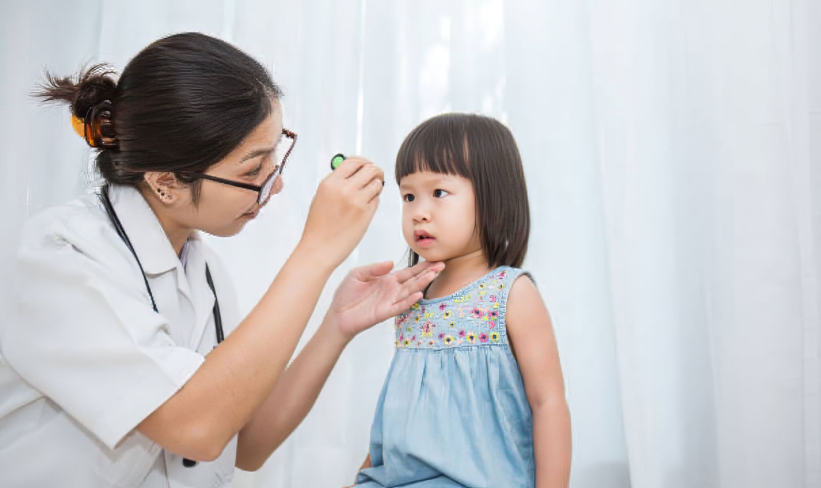 Asian eye doctor performing an eye exam on an asian toddler.
